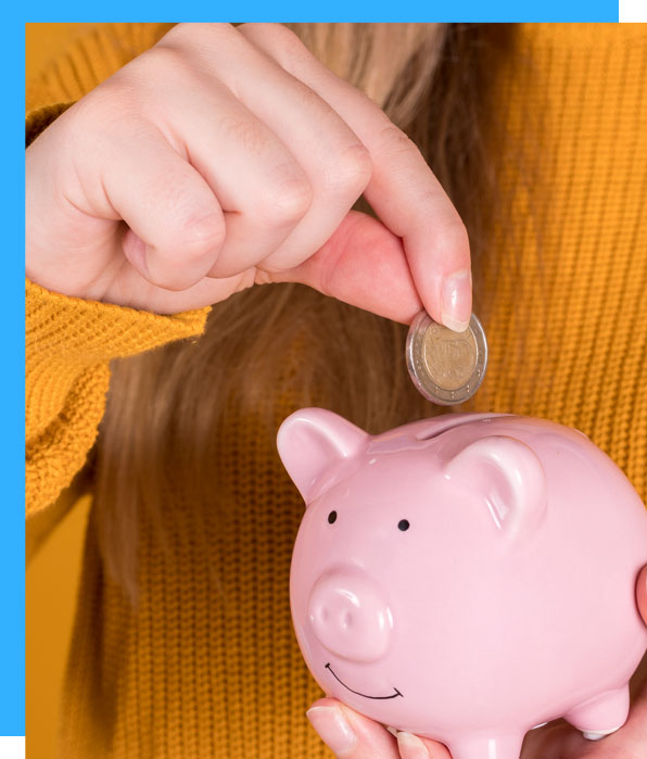 Hand inserting a coin into a pink piggy bank against a yellow background.